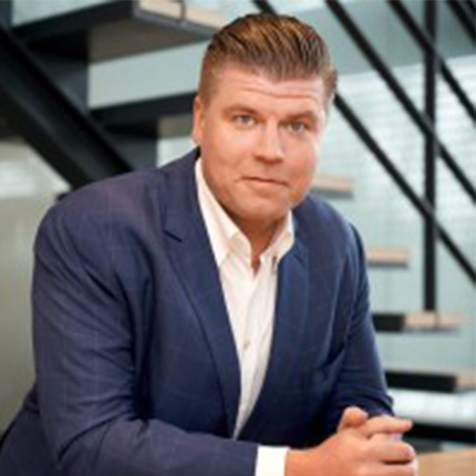 Lukas Heise, CEO der Fischbach Gruppe lehnt an einem Tisch vor einem hellen Treppenaufgang eines Bürogebäudes